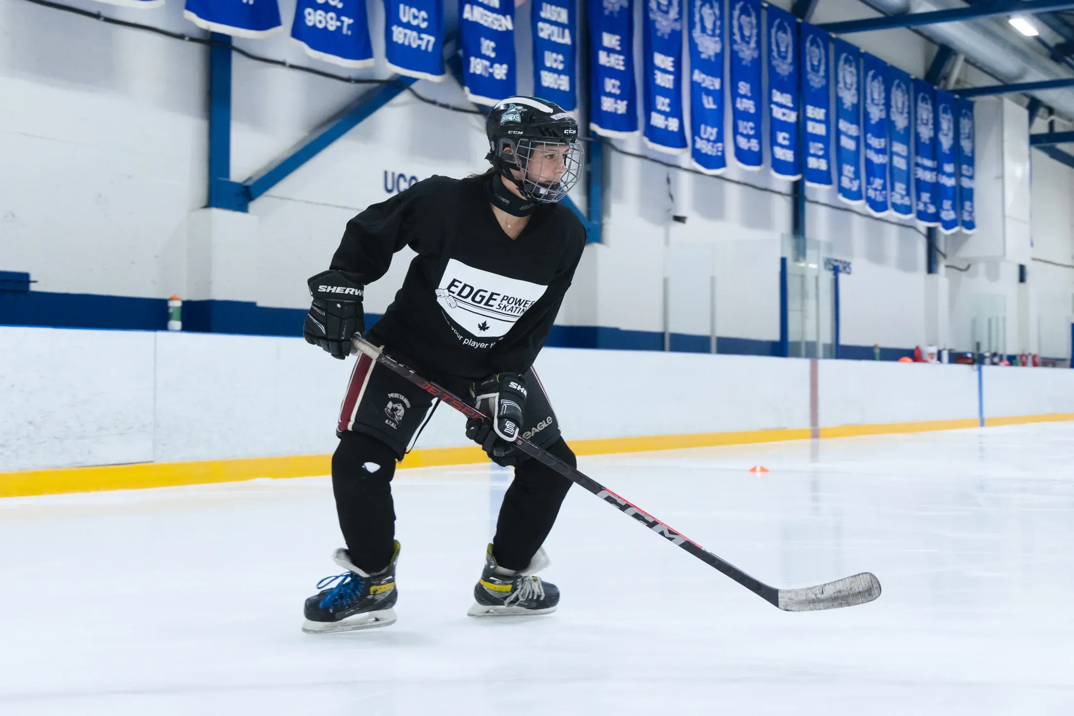 An older Edge player in a deep athletic stance, UCC alumni banners overhead